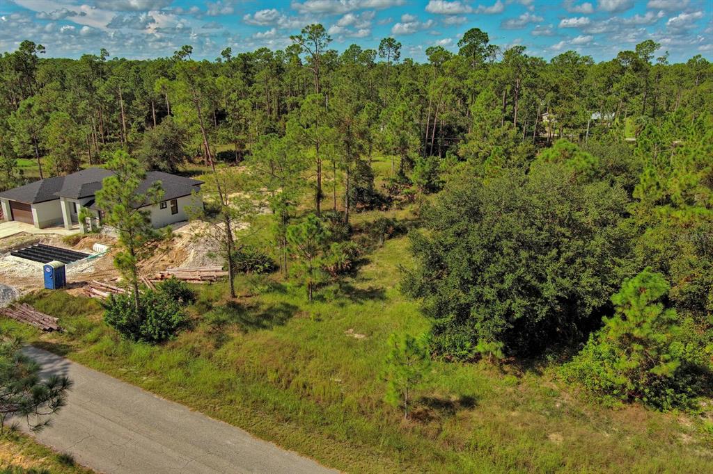 An aerial view shows a house under construction next to a wooded, grassy lot — 1219 WASHINGTON AVENUE, LEHIGH ACRES, FL