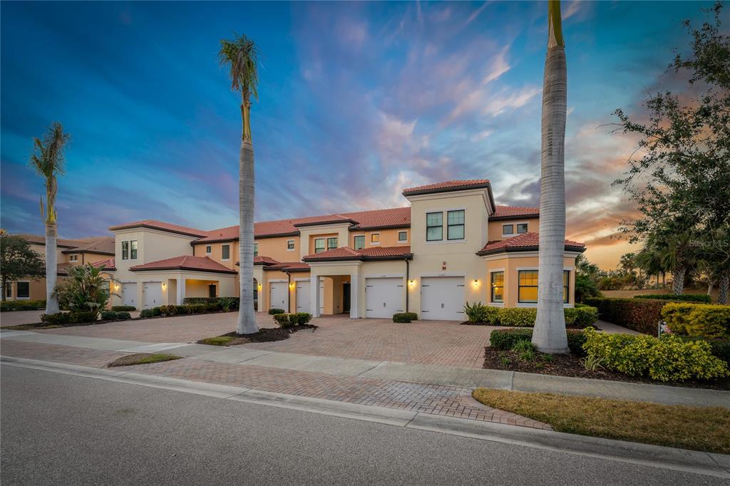 A multi-unit residential building with a paved driveway, palm trees, and a tiled roof — 23085 BANBURY WAY UNIT 103, VENICE, FL
