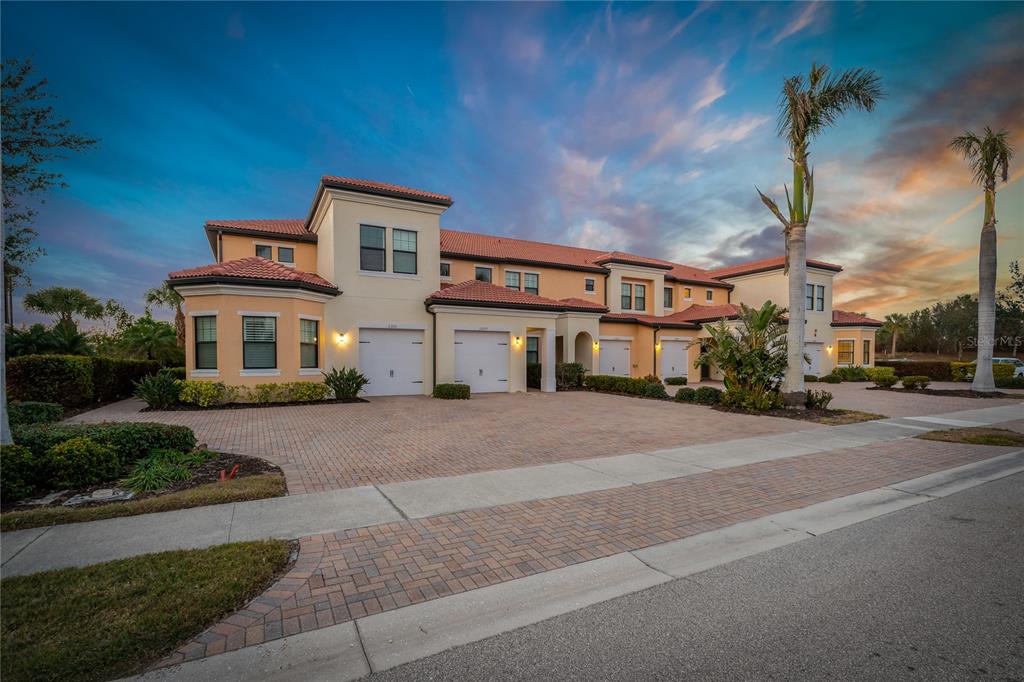 A multi-unit residential building with a paved driveway and palm trees at sunset — 23085 BANBURY WAY UNIT 103, VENICE, FL