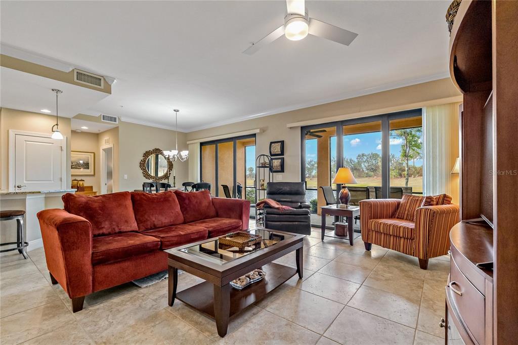 A living room features a red sofa, tile flooring, and sliding glass doors overlooking a landscape — 23085 BANBURY WAY UNIT 103, VENICE, FL