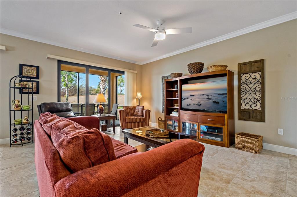 A living room features a red sofa, a wooden entertainment center, and a sliding glass door — 23085 BANBURY WAY UNIT 103, VENICE, FL