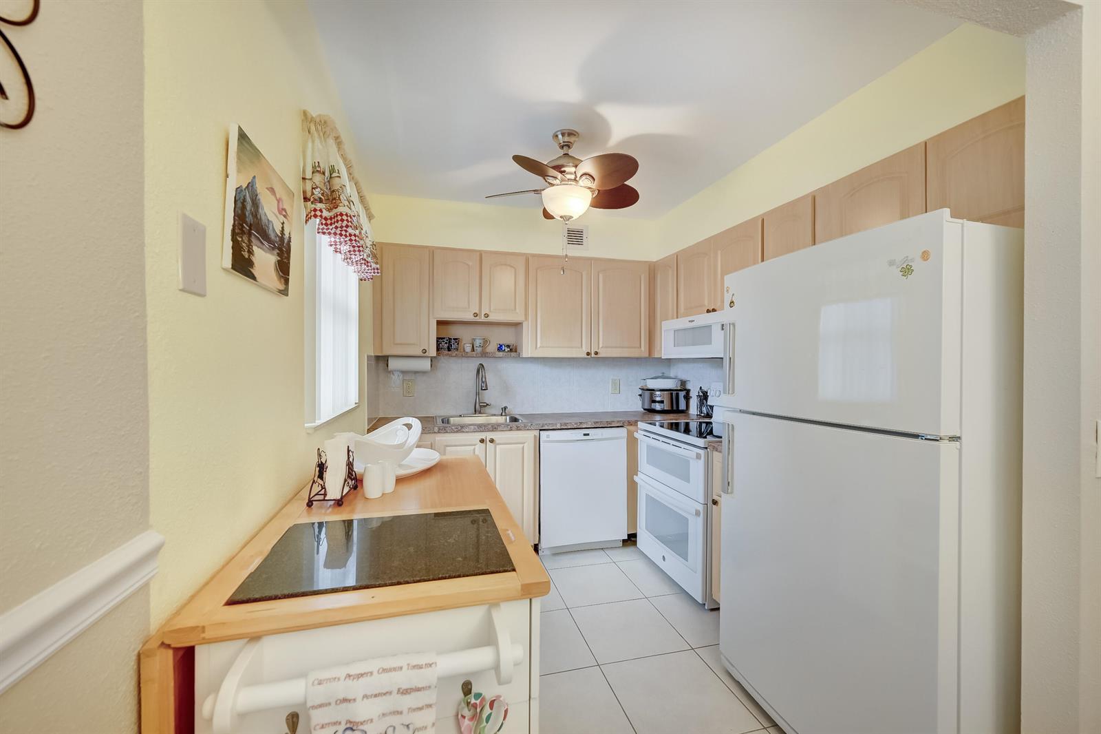A kitchen features light wood cabinets, white appliances, tile flooring, and a small island — 601 Monaco M # M, Delray Beach FL 33446, DELRAY BEACH, FL