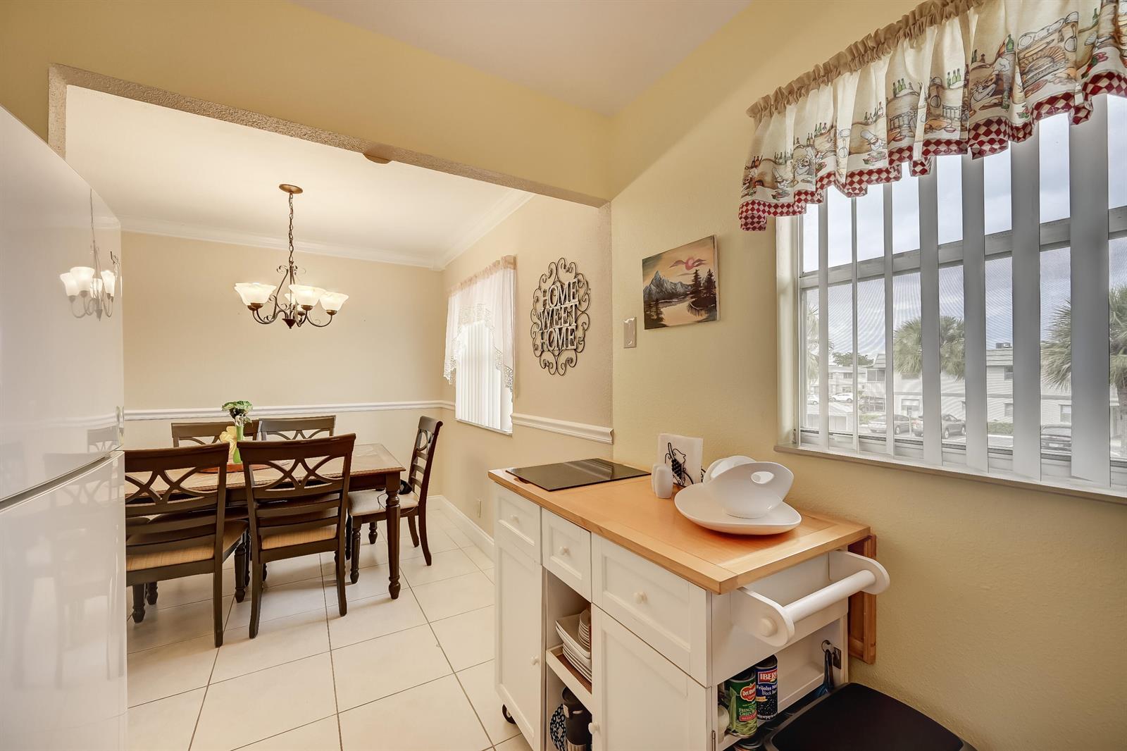 A dining area with a wooden table and chairs sits adjacent to a kitchen island — 601 Monaco M # M, Delray Beach FL 33446, DELRAY BEACH, FL