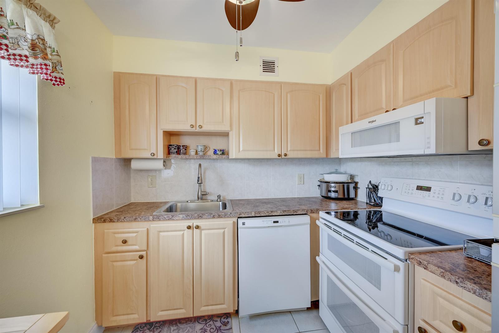 A kitchen features light wood cabinets, white appliances, a stainless steel sink, and tiled backsplash — 601 Monaco M # M, Delray Beach FL 33446, DELRAY BEACH, FL