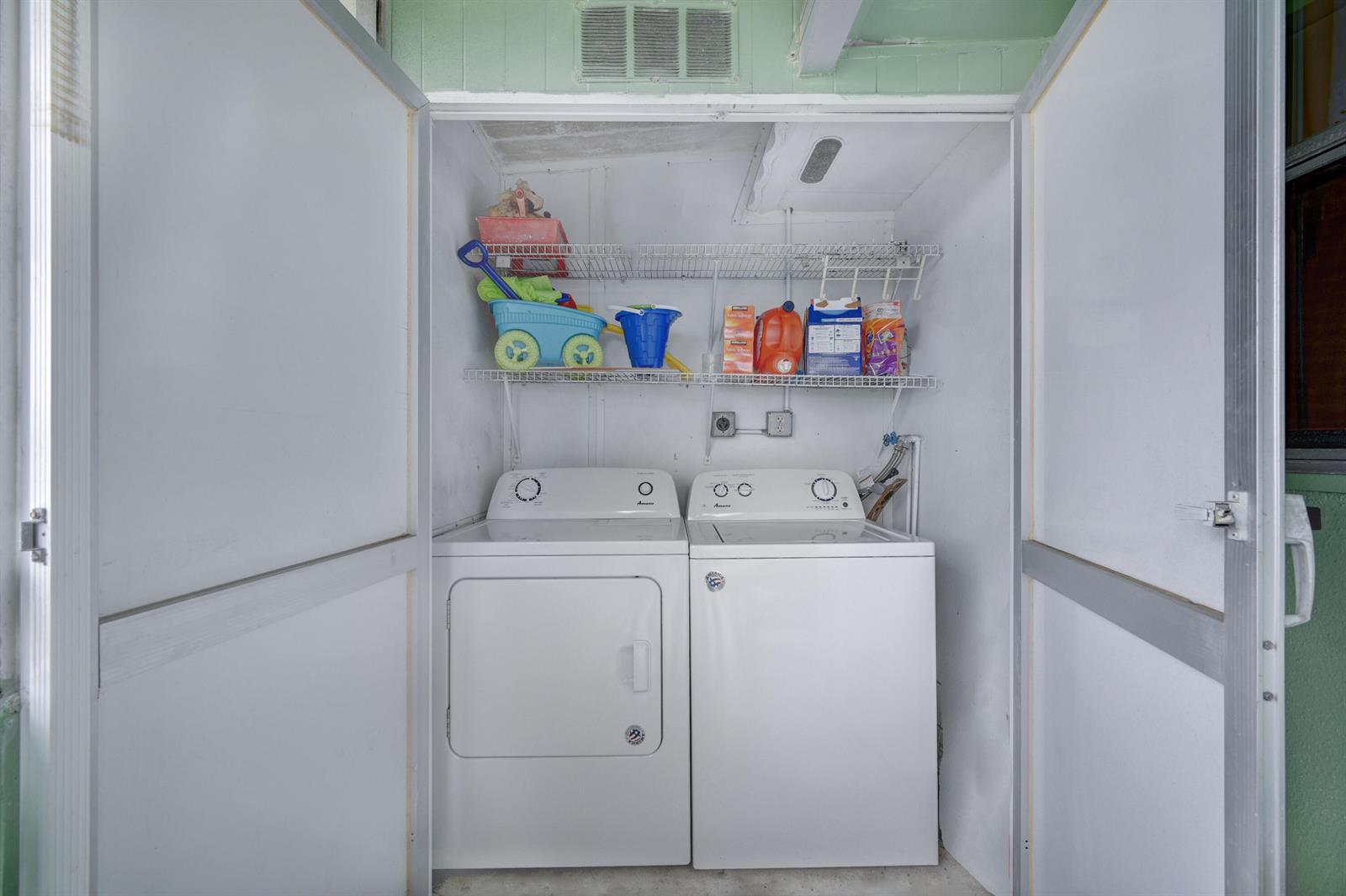 A laundry closet contains a white washer and dryer beneath a wire storage shelf — 601 Monaco M # M, Delray Beach FL 33446, DELRAY BEACH, FL