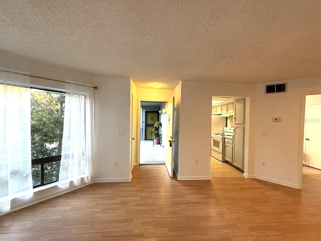 A living room with light wood-look flooring leads to an open kitchen and exterior entryway — 4308 LAKEWAY DRIVE UNIT E (50), ORLANDO, FL