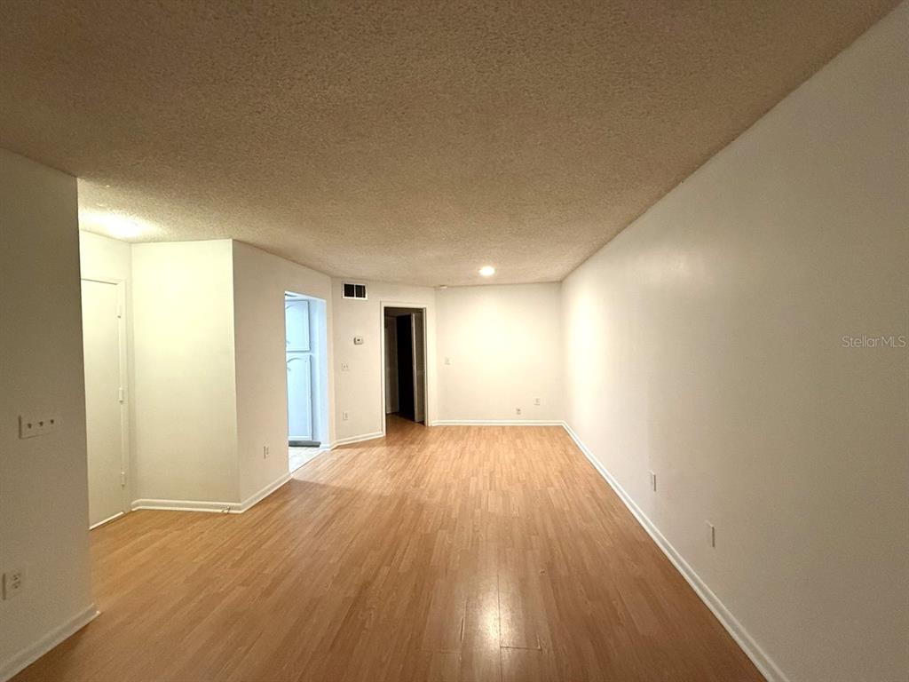 An empty living room features light wood-look flooring, white walls, and a textured ceiling — 4308 LAKEWAY DRIVE UNIT E (50), ORLANDO, FL