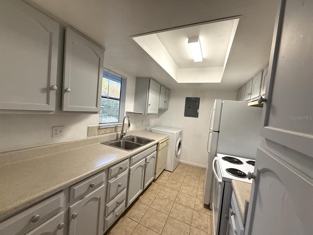 A kitchen features white cabinets, light countertops, a double sink, and an adjacent laundry area — 4308 LAKEWAY DRIVE UNIT E (50), ORLANDO, FL