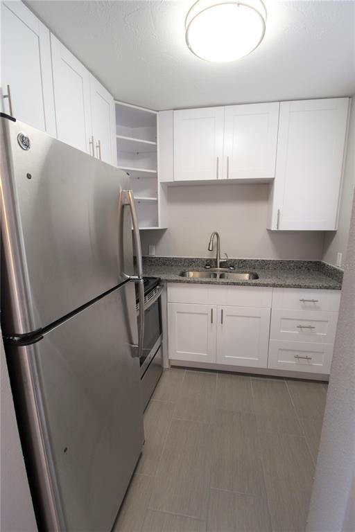 A kitchen features white cabinets, stainless steel appliances, granite countertops, and light gray tile flooring — 3001 BEE RIDGE ROAD UNIT 215, SARASOTA, FL