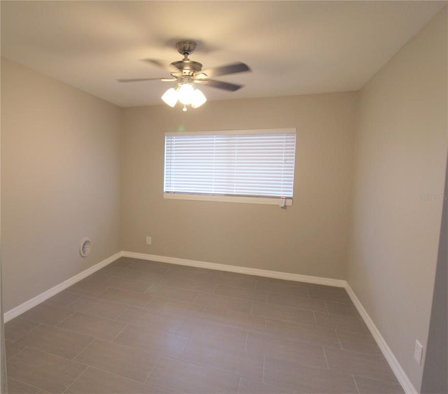 An empty room with light gray walls, tile flooring, a ceiling fan, and a window — 3001 BEE RIDGE ROAD UNIT 215, SARASOTA, FL