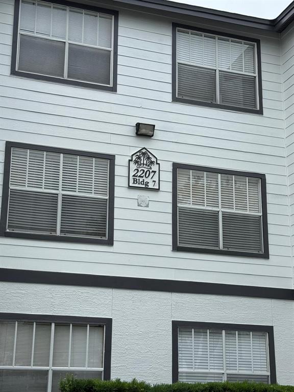 The exterior of a multi-story apartment building features white horizontal siding and dark-framed windows — 2207 ANTIGUA PLACE UNIT 727, KISSIMMEE, FL