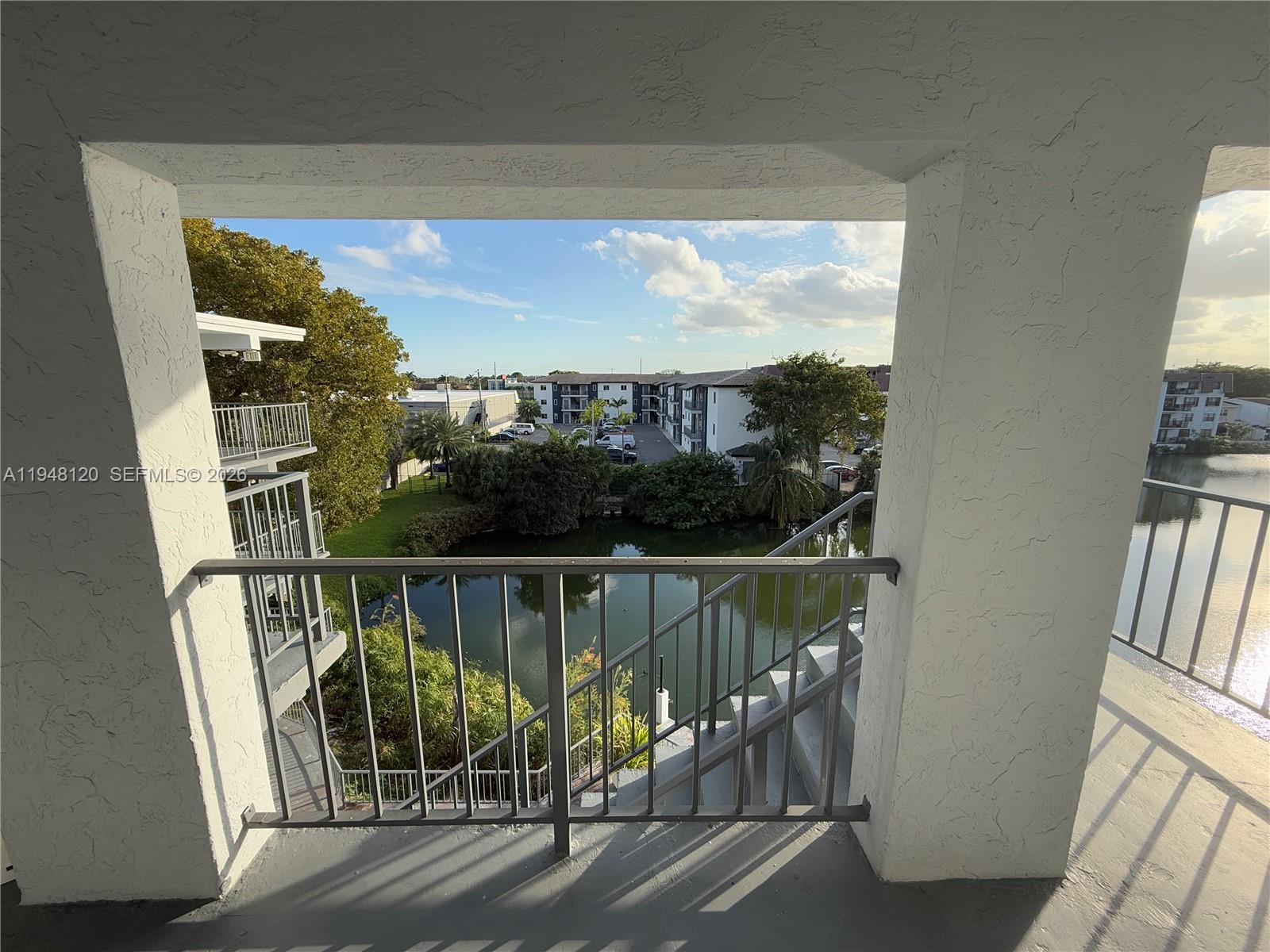 A balcony view overlooks a small pond, stairs, and surrounding apartment buildings under a blue sky — 7105 W 13th Ave # 402, Hialeah FL 33014, HIALEAH, FL