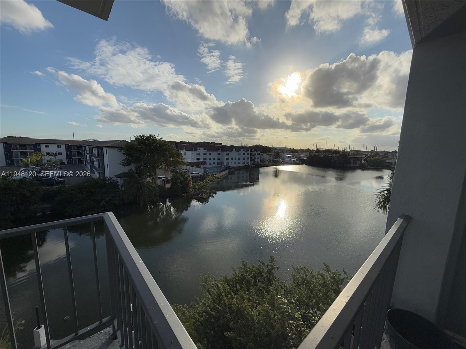 A balcony overlooks a lake surrounded by apartment buildings under a cloudy sky — 7105 W 13th Ave # 402, Hialeah FL 33014, HIALEAH, FL