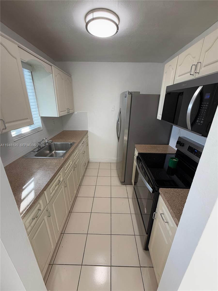 A galley kitchen features white cabinets, granite countertops, stainless steel appliances, and tiled flooring — 7105 W 13th Ave # 402, Hialeah FL 33014, HIALEAH, FL