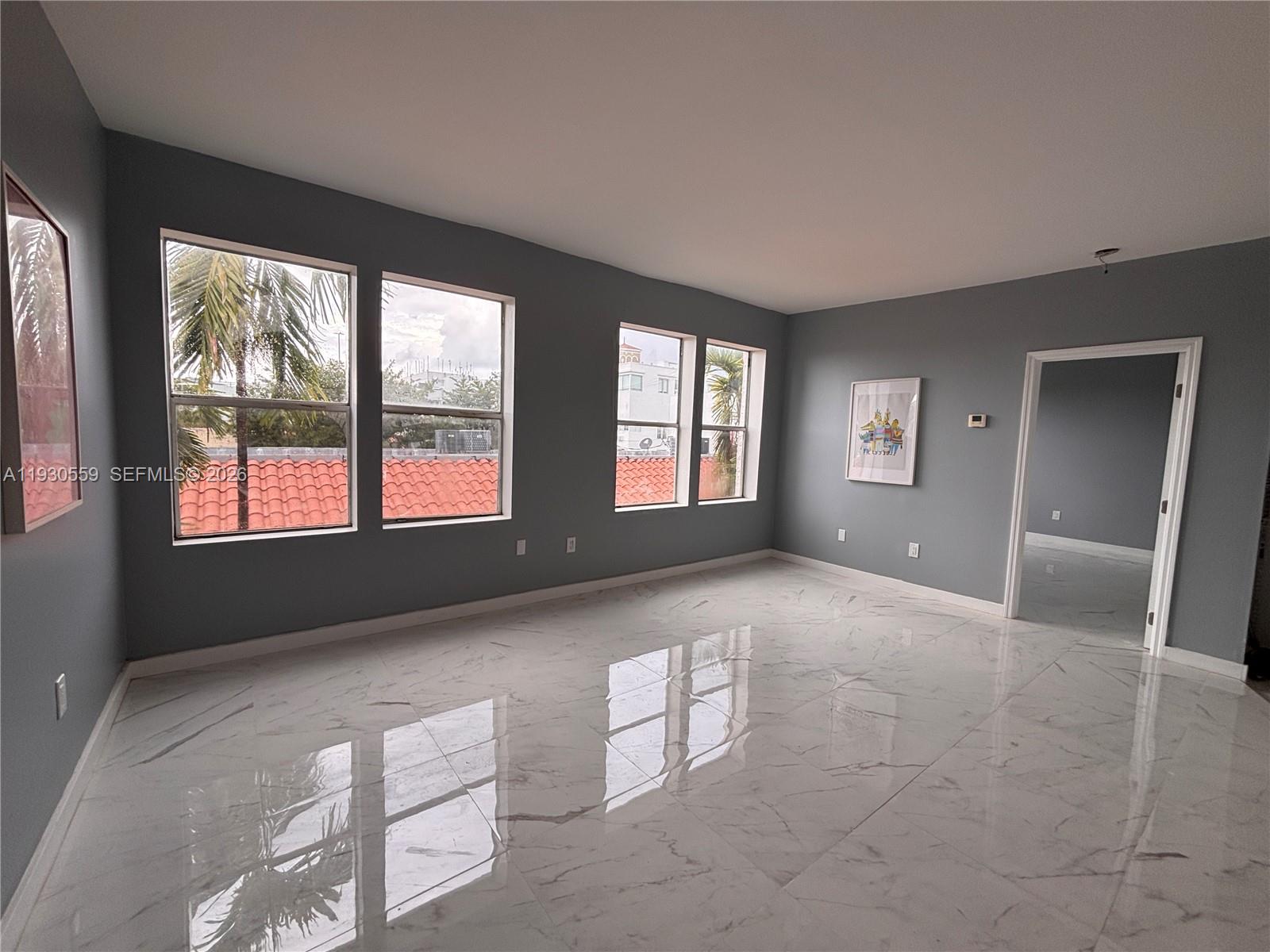 An empty room features gray walls, white marble-look tile flooring, and four windows overlooking rooftops — 1027 Pennsylvania Ave # 302, Miami Beach FL 33139, MIAMI BEACH, FL