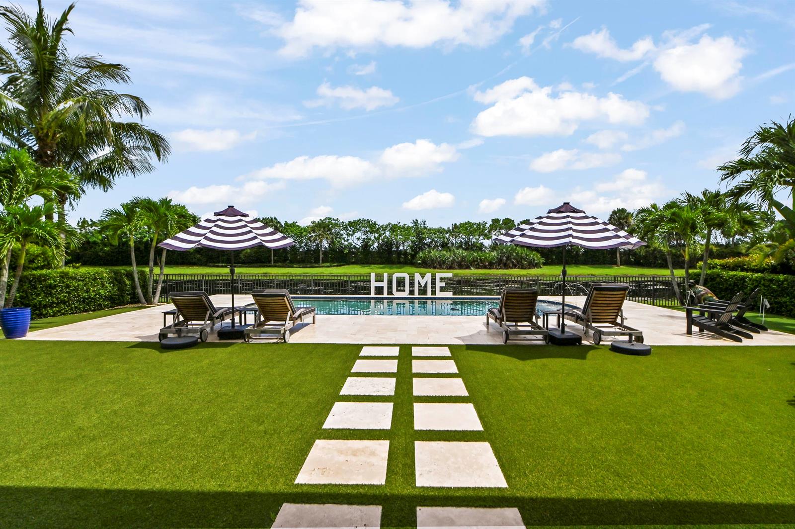A backyard features a swimming pool, lounge chairs under striped umbrellas, and a stone walkway — 9307 Grand Prix Lane, Boynton Beach FL 33472, BOYNTON BEACH, FL