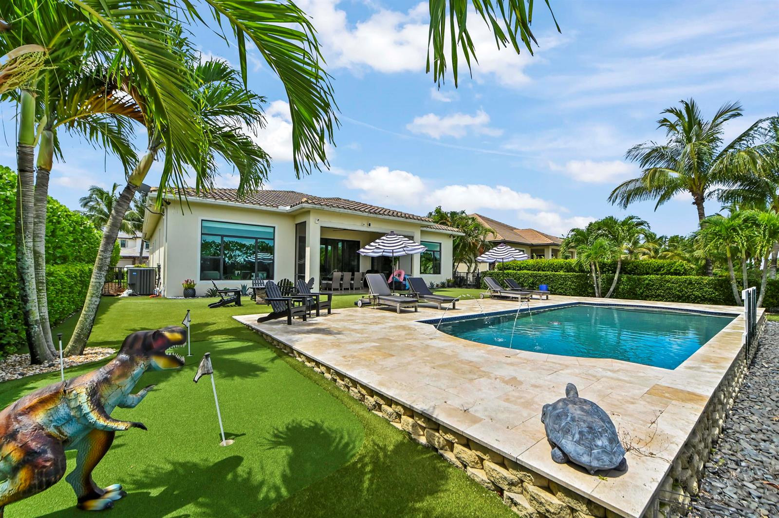 A backyard with a swimming pool, putting green, dinosaur statue, and patio furniture — 9307 Grand Prix Lane, Boynton Beach FL 33472, BOYNTON BEACH, FL