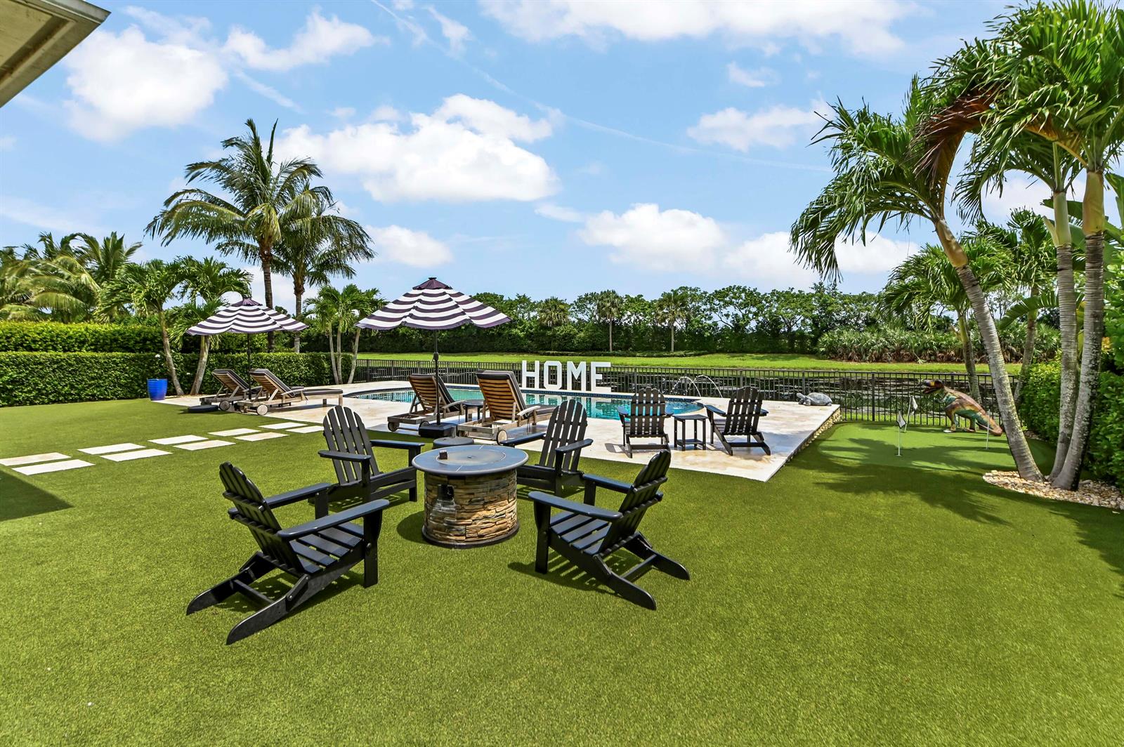 A backyard features a swimming pool, a fire pit with chairs, and a putting green — 9307 Grand Prix Lane, Boynton Beach FL 33472, BOYNTON BEACH, FL