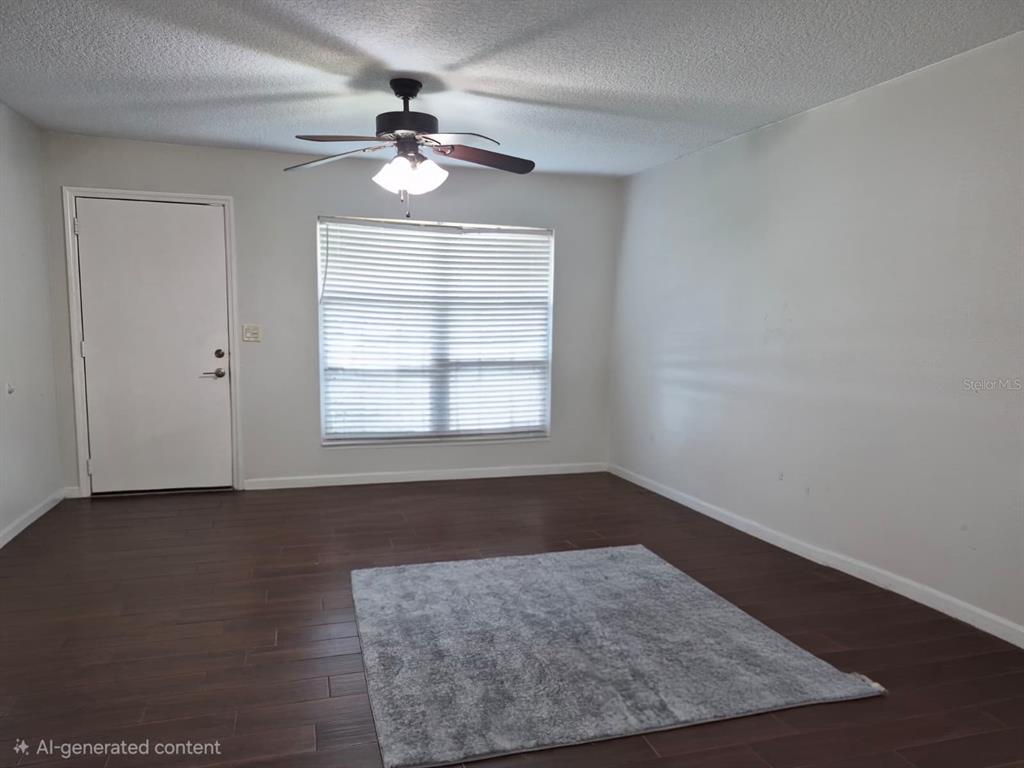 An empty room features dark wood-look flooring, a ceiling fan, and a gray area rug — 2729 HARRIET DRIVE, ORLANDO, FL