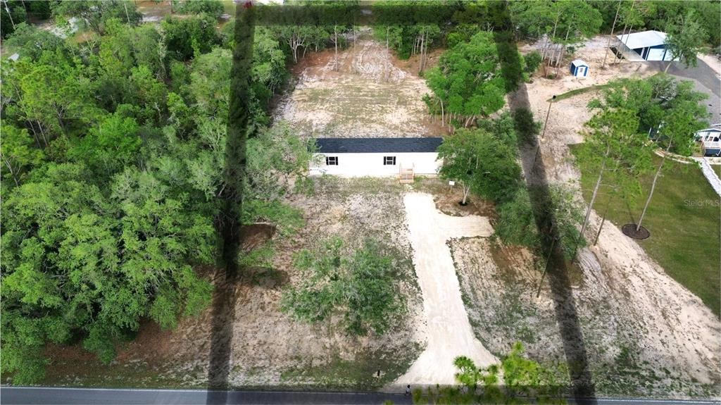 An aerial view shows a rectangular manufactured home situated on a large, partially cleared lot — 8851 NE 105TH AVENUE, BRONSON, FL