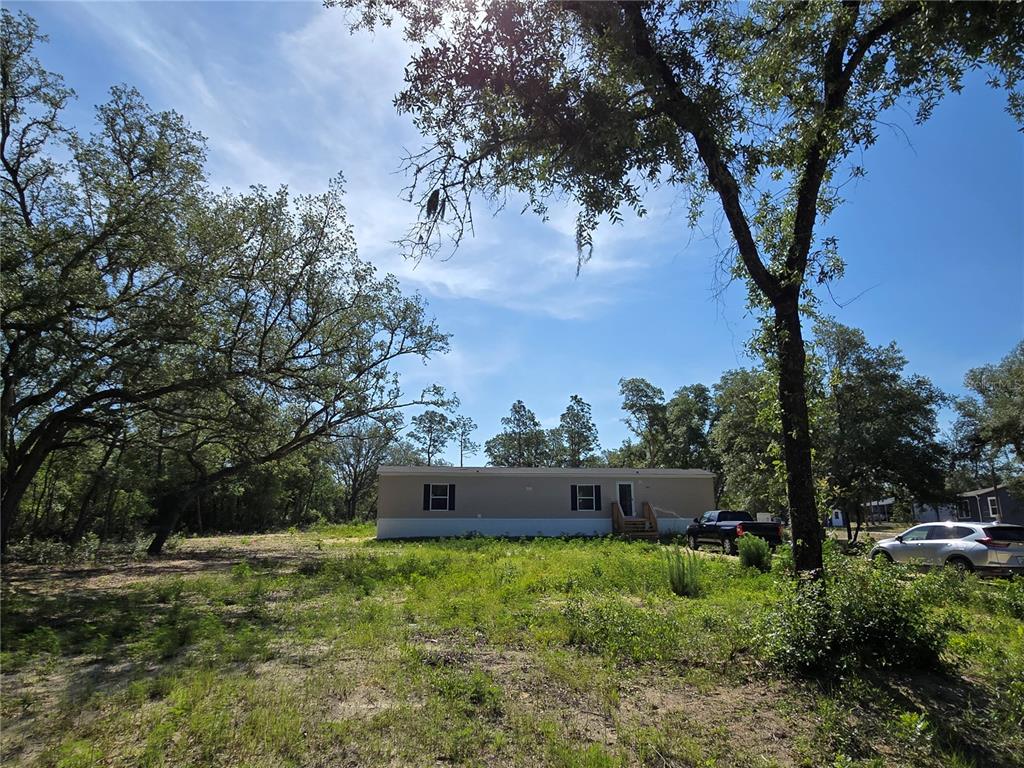 A single-story manufactured home sits on a grassy lot surrounded by trees under a blue sky — 8851 NE 105TH AVENUE, BRONSON, FL