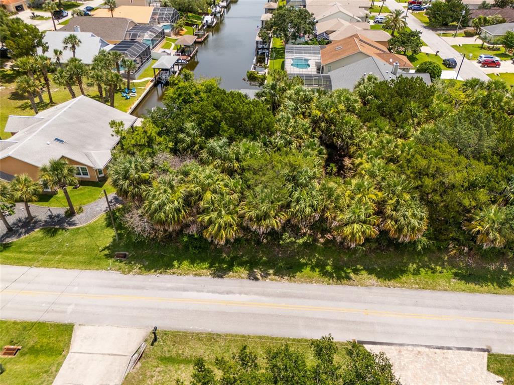 An aerial view shows a vacant, wooded lot situated between a house and a canal — 34 COCHISE COURT, PALM COAST, FL