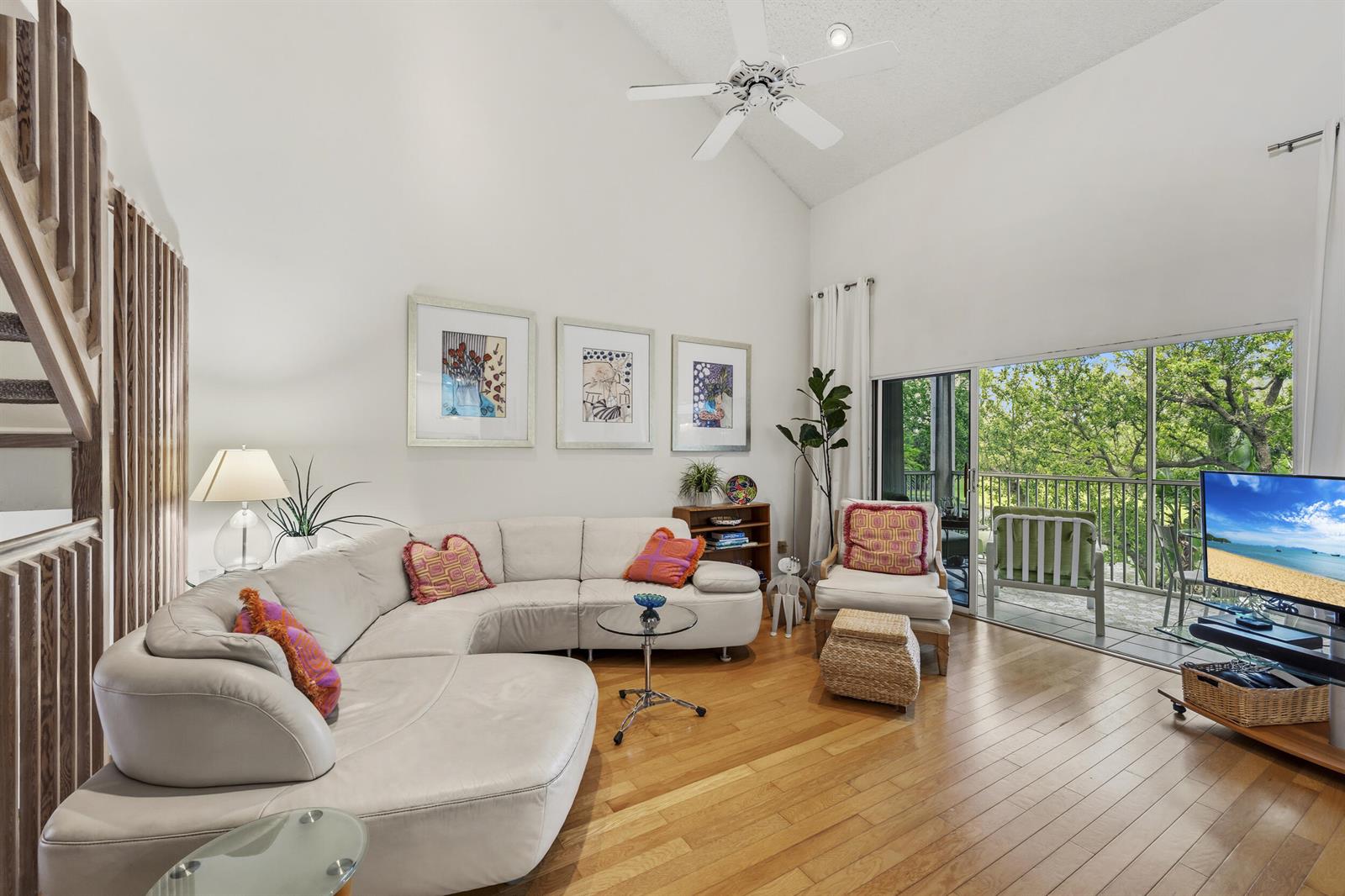 A living room with a white sectional sofa, vaulted ceiling, hardwood floors, and a balcony view — 2506 N Fairway Drive N, Jupiter FL 33477, JUPITER, FL
