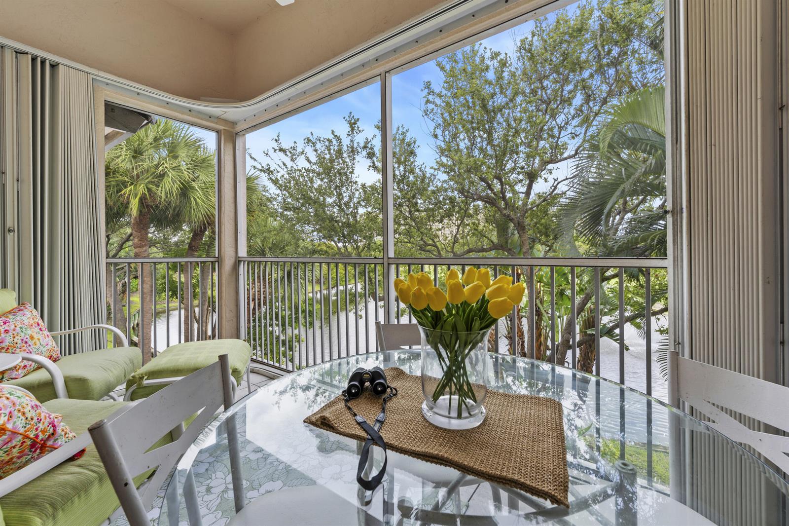 A screened-in balcony features a glass dining table, yellow tulips, and views of a lake — 2506 N Fairway Drive N, Jupiter FL 33477, JUPITER, FL
