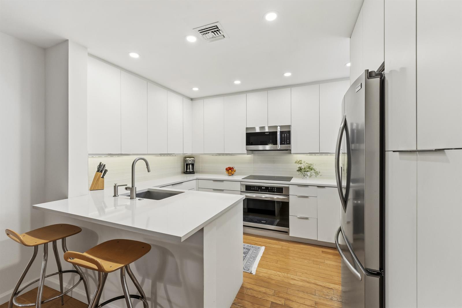A modern kitchen features white cabinetry, stainless steel appliances, a peninsula, and hardwood flooring — 2506 N Fairway Drive N, Jupiter FL 33477, JUPITER, FL