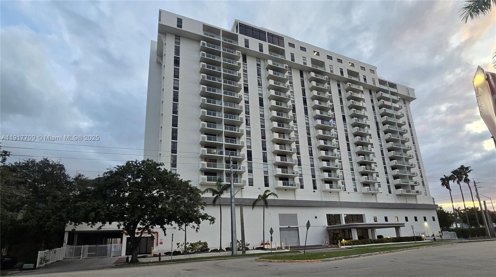 A tall, white multi-story apartment building features numerous balconies and a ground-level parking entrance — 13499 Biscayne Blvd, North Miami FL 33181, NORTH MIAMI, FL