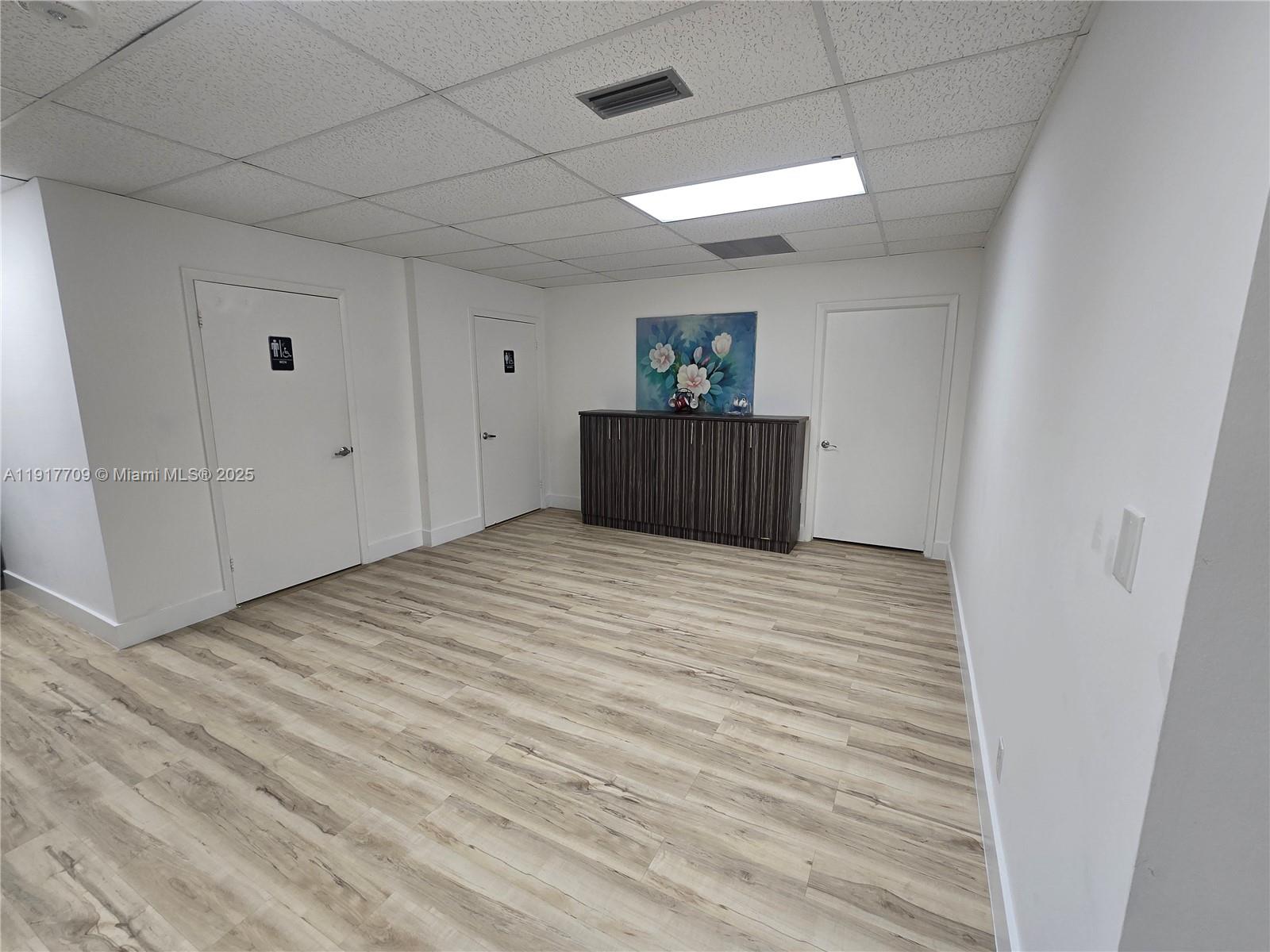 An interior room features white walls, wood-look flooring, a drop ceiling, and three closed doors — 13499 Biscayne Blvd, North Miami FL 33181, NORTH MIAMI, FL