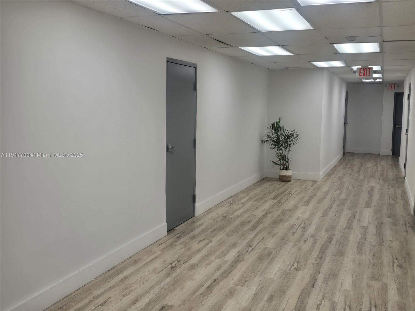 A hallway with white walls, wood-look flooring, a gray door, and a potted plant — 13499 Biscayne Blvd, North Miami FL 33181, NORTH MIAMI, FL