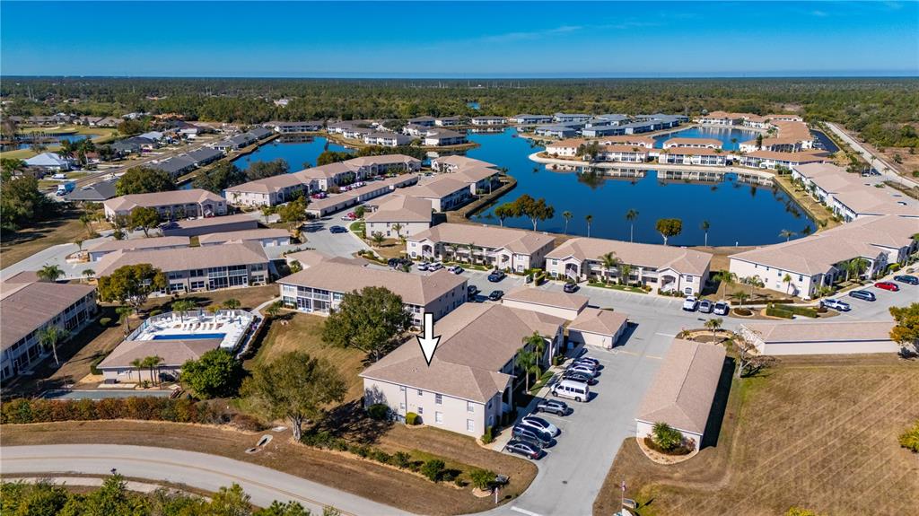 An aerial view shows a multi-story apartment building complex with a swimming pool and lake — 11644 SW EGRET CIRCLE UNIT 1205, LAKE SUZY, FL