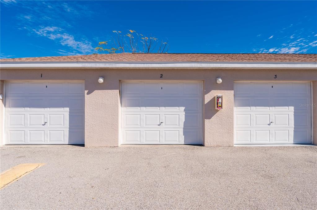 A row of three white garage doors on a tan building under a blue sky — 11644 SW EGRET CIRCLE UNIT 1205, LAKE SUZY, FL