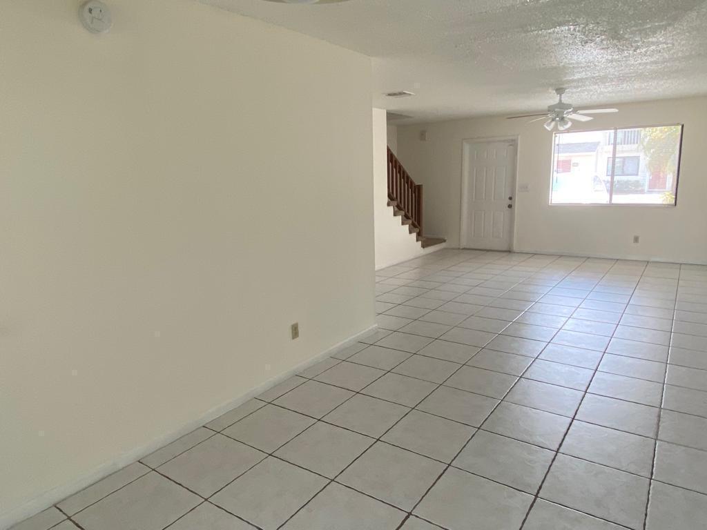 An empty living room with white walls, light-colored tile flooring, a ceiling fan, and stairs — 4901 Pier Drive, FL 33463, FL