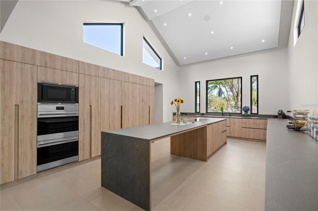 A modern kitchen features light wood cabinetry, a large dark stone island, and vaulted ceilings — 111 DORADO BEACH EAST, DORADO, PR
