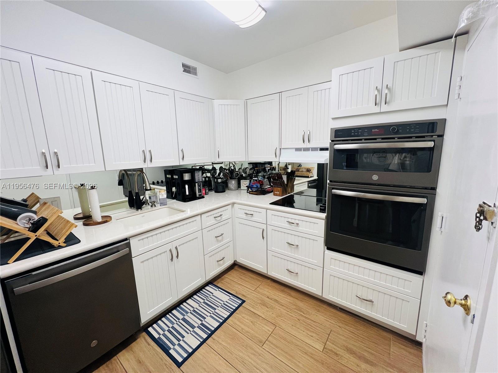 A kitchen features white beadboard cabinetry, stainless steel appliances, and wood-look tile flooring — 1980 S Ocean Dr # 9M, Hallandale Beach FL 33009, HALLANDALE BEACH, FL
