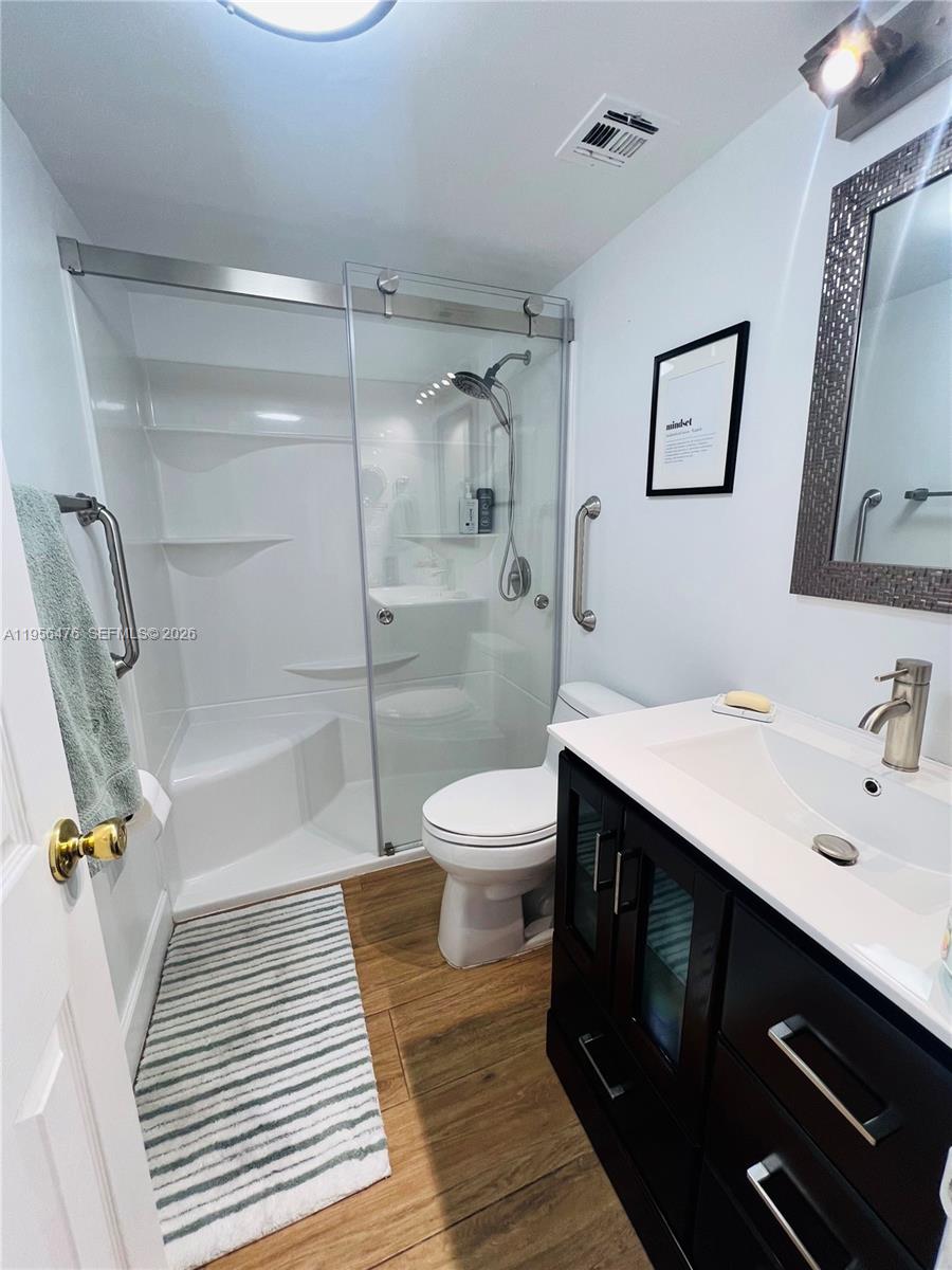 A bathroom features a glass-enclosed shower, a dark wood vanity, and wood-look flooring — 1980 S Ocean Dr # 9M, Hallandale Beach FL 33009, HALLANDALE BEACH, FL