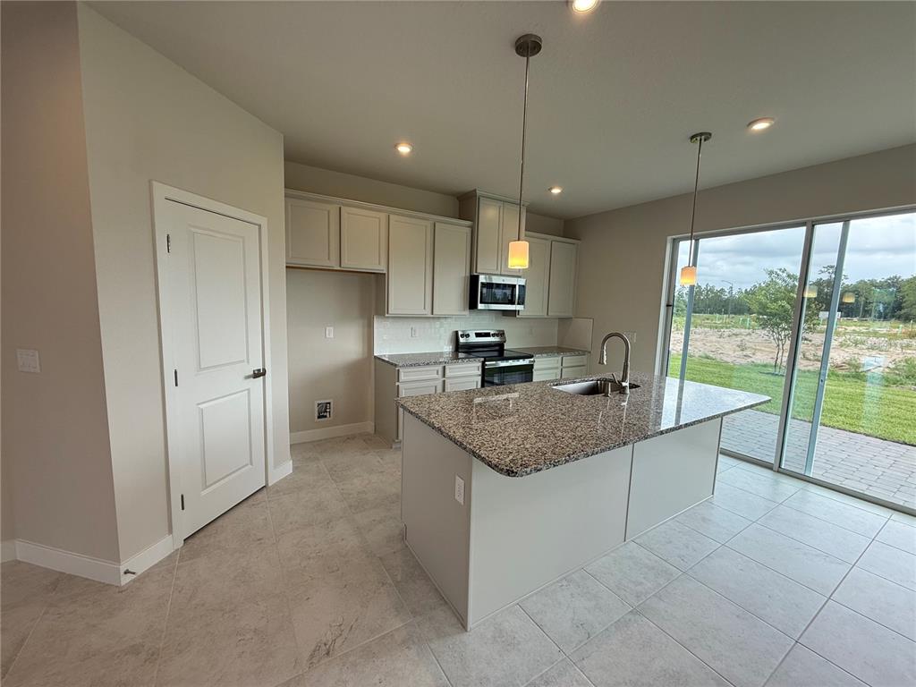 A kitchen features light-colored cabinets, granite countertops, a center island, and sliding glass doors — 1253 PINEYWOOD FIELD DRIVE, DAVENPORT, FL