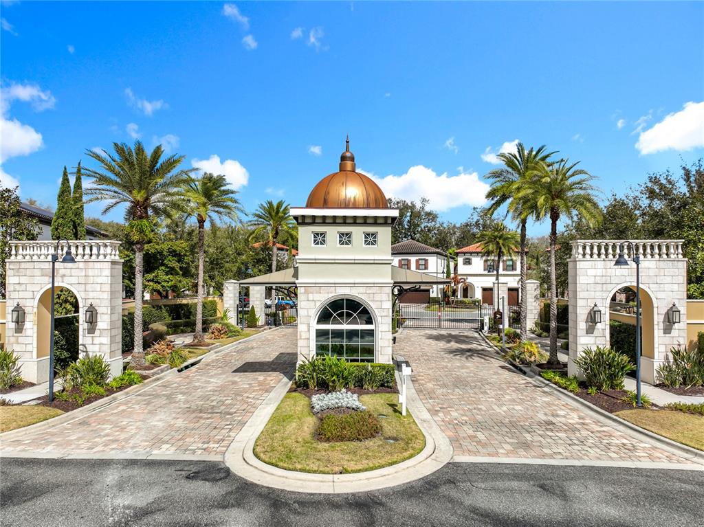 A gated entrance features a stone guardhouse with a copper dome and palm trees — 8358 VIA VITTORIA WAY, ORLANDO, FL