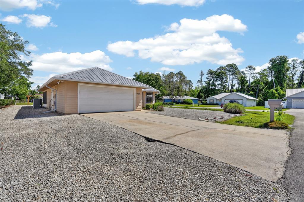 A tan house with a metal roof and a concrete driveway sits on a gravel lot — 7200 ANDREW JACKSON STREET, PALATKA, FL