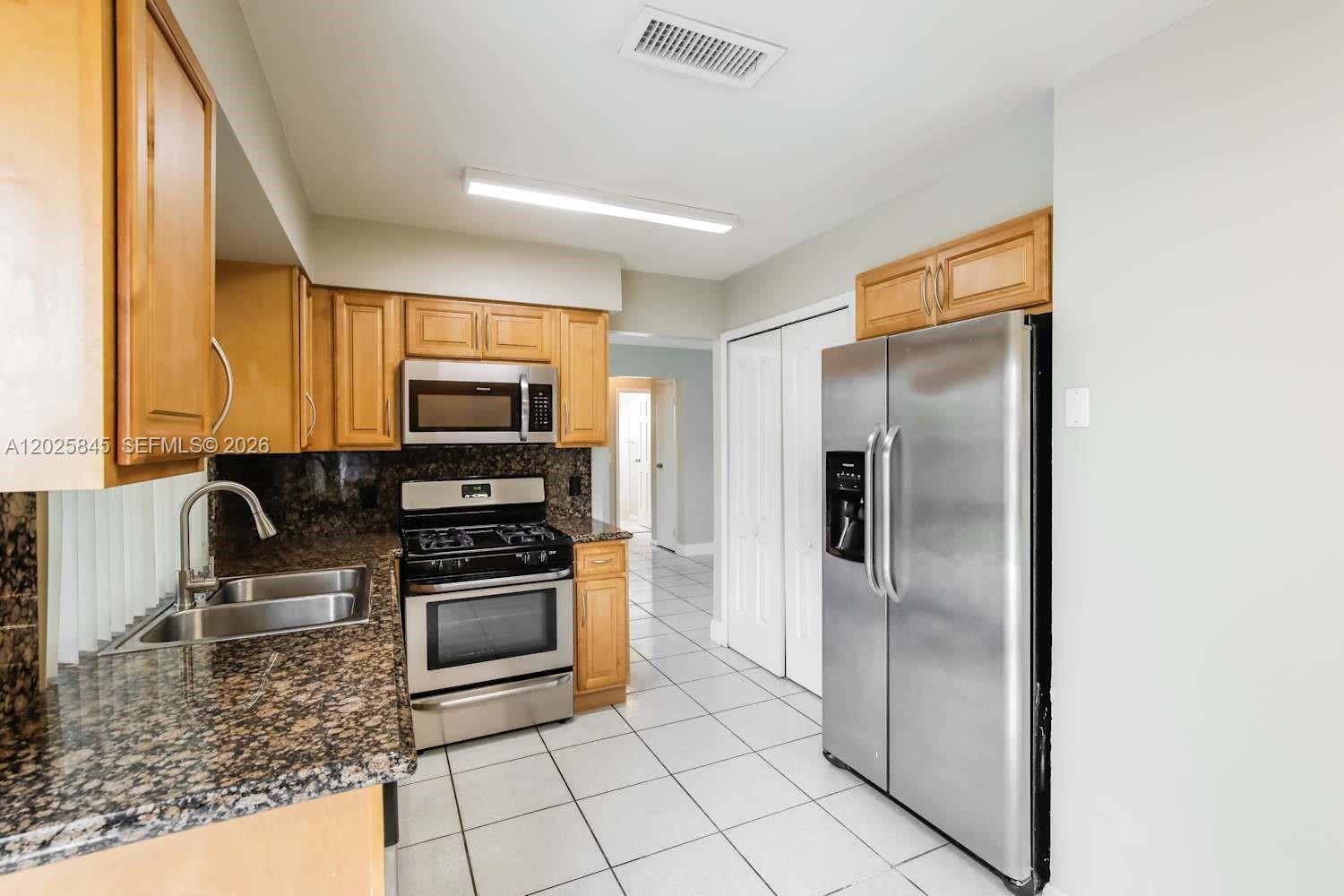 A kitchen features light wood cabinets, granite countertops, stainless steel appliances, and white tile flooring — SUNRISE, FL