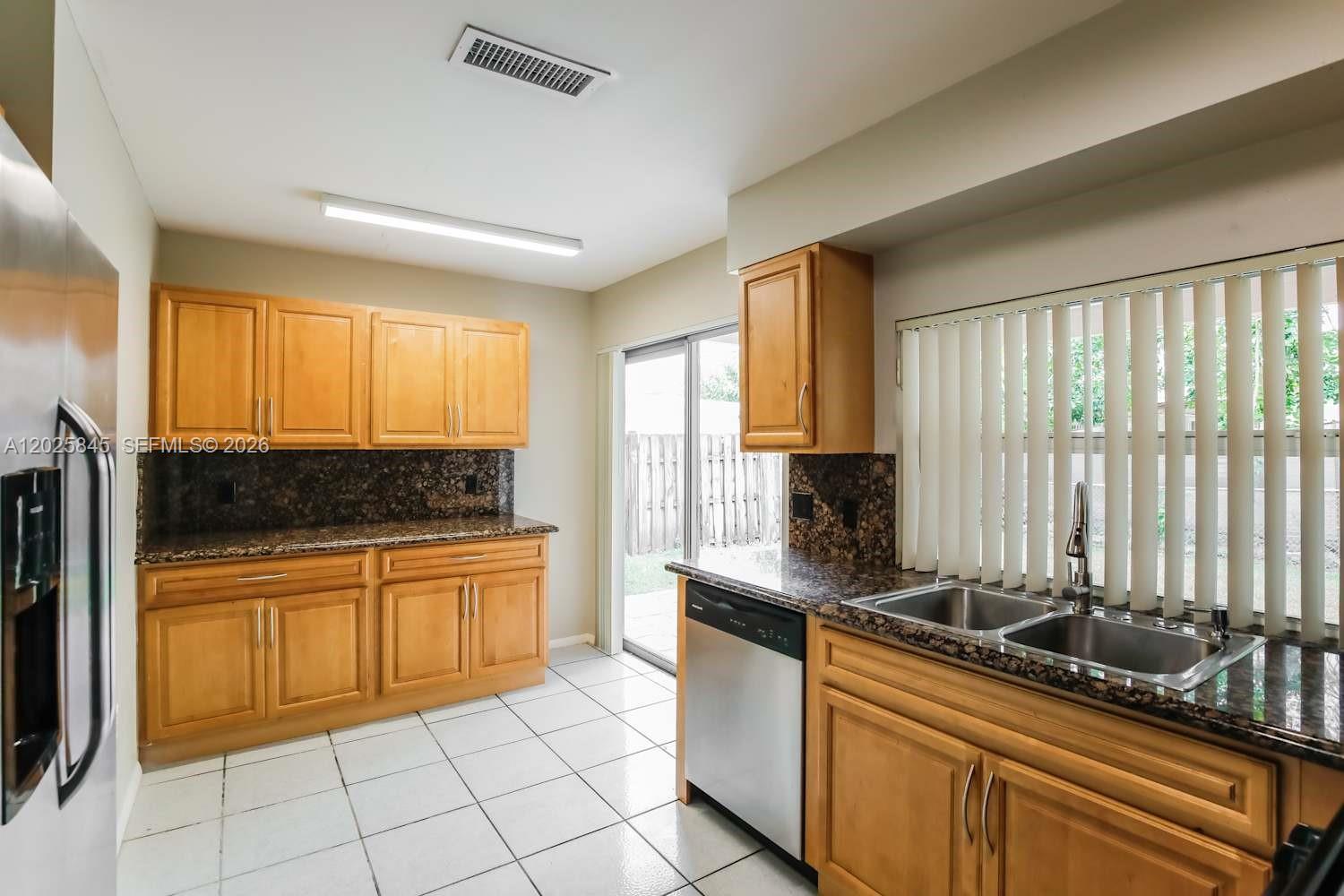 A kitchen features light wood cabinets, dark granite countertops, stainless steel appliances, and tile flooring — SUNRISE, FL