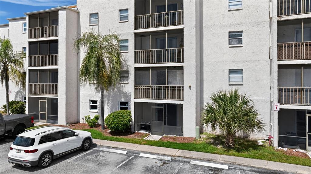 A multi-story apartment building exterior with screened balconies, a parking lot, and palm trees — 5541 BAY BOULEVARD UNIT 203, PORT RICHEY, FL