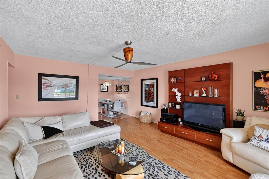 A living room with a white sectional sofa, wood-look flooring, and a large media wall unit — 5541 BAY BOULEVARD UNIT 203, PORT RICHEY, FL