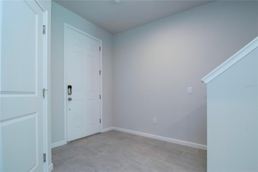 An entryway features light gray walls, tile flooring, a white door, and a staircase railing — 11518 ROLLING GREEN DRIVE, BRADENTON, FL