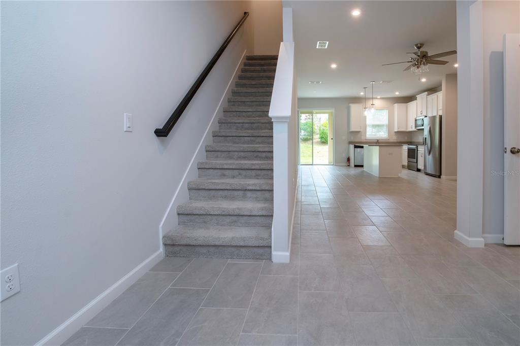 A carpeted staircase leads to an upper floor beside an open-concept kitchen and living area — 11518 ROLLING GREEN DRIVE, BRADENTON, FL