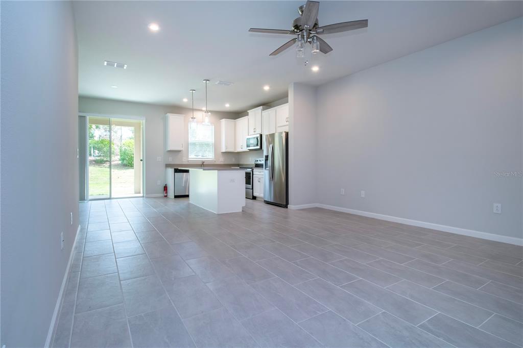 An open-concept kitchen and living area feature light gray tile flooring and white cabinetry — 11518 ROLLING GREEN DRIVE, BRADENTON, FL