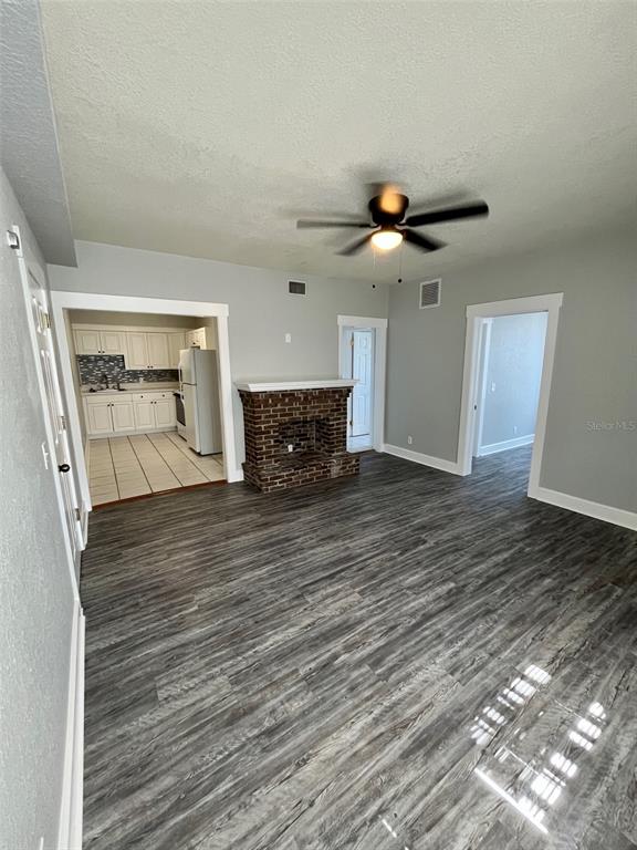 A living room features a brick fireplace, gray wood-look flooring, and a view into the kitchen — 644 4TH AVENUE S, ST PETERSBURG, FL