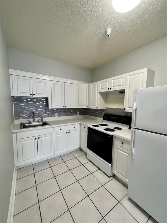 A kitchen features white cabinets, a tiled backsplash, white appliances, and light-colored floor tiles — 644 4TH AVENUE S, ST PETERSBURG, FL